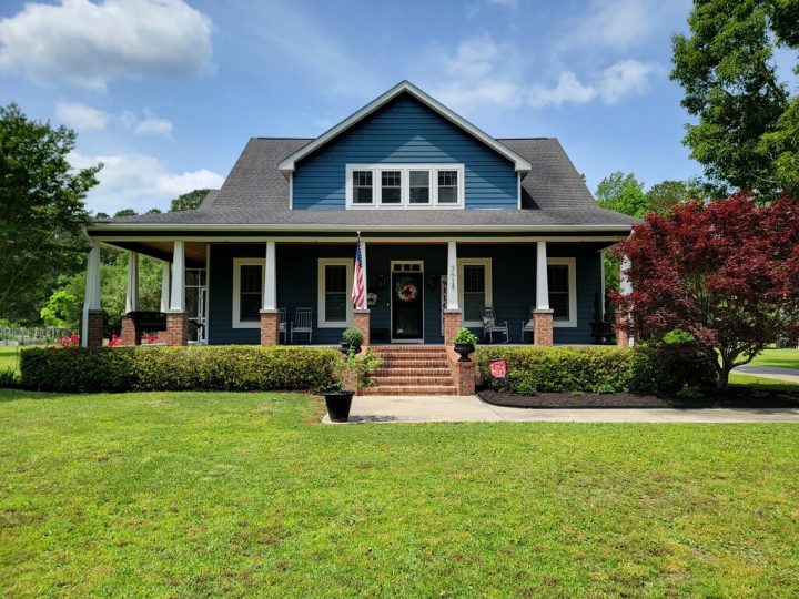 Beautifully maintained front lawn with lush green grass, trimmed shrubs, and a neat landscape in front of a blue house after fertilization and weed control services by Home and Lawn Hero.