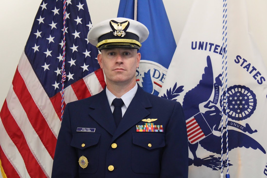 John Walton Sr., U.S. Coast Guard member in full dress uniform, standing in front of American and military flags, representing the veteran leadership behind Home and Lawn Hero