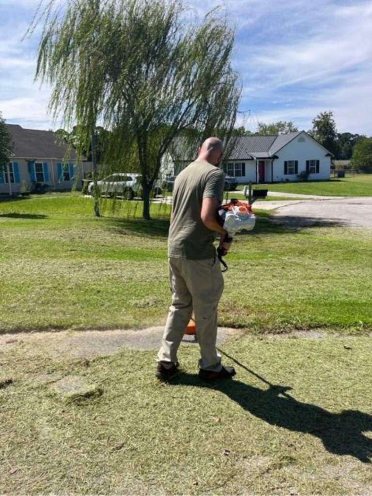 Home and Lawn Hero team member using a string trimmer for precision edging during residential lawn maintenance service in Pender County, North Carolina