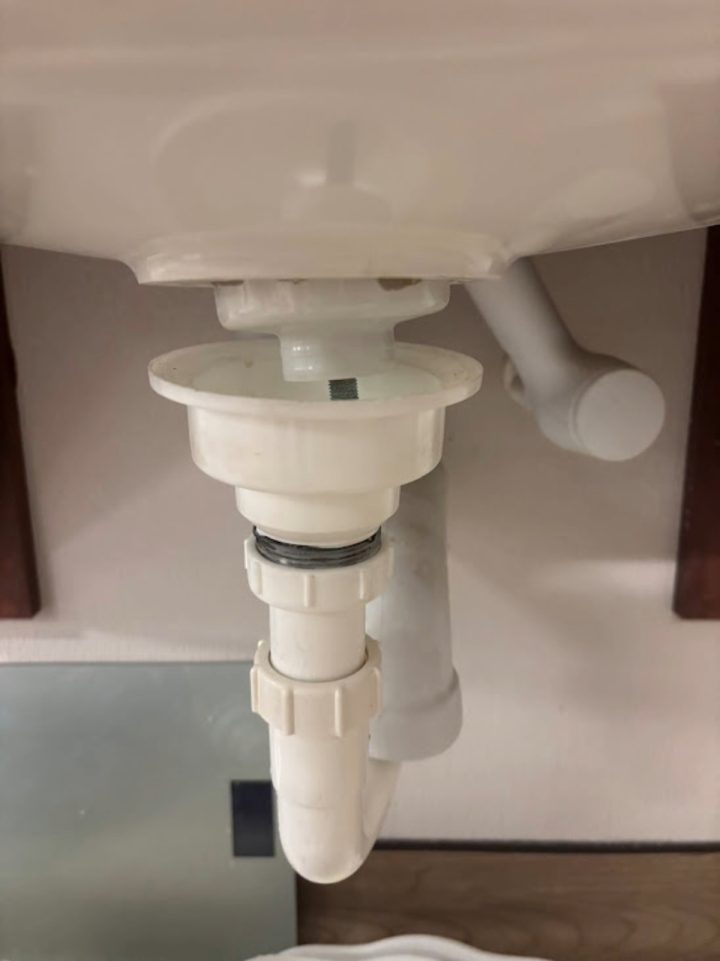 Close-up of white PVC sink drain pipe and P-trap under bathroom sink showing plumbing repair work.