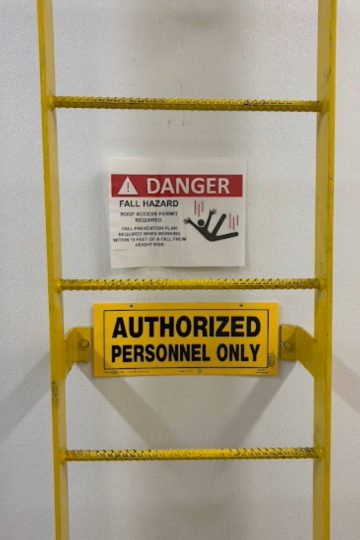 Yellow safety ladder with danger fall hazard sign and authorized personnel only warning in commercial property maintenance area.