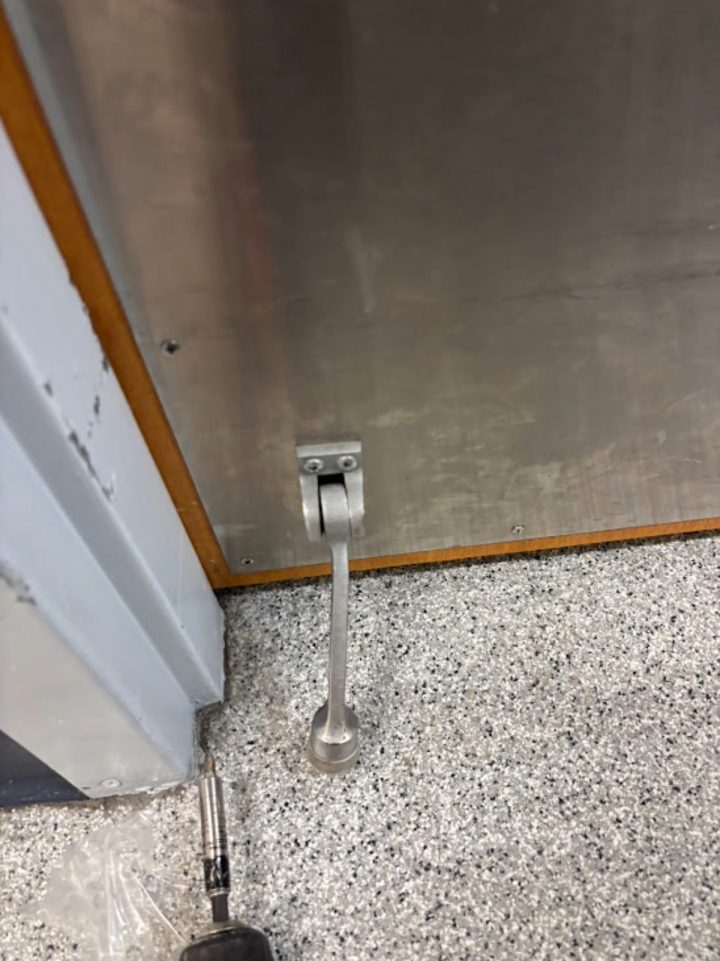 Commercial door stopper hardware attached to metal door with screwdriver on the floor nearby